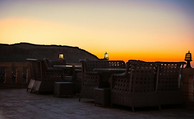 Outdoor terrace set for an evening gathering at sunset, lanterns glowing against an amber sky