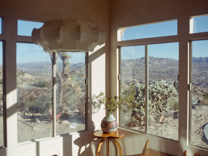 Film photograph of a desert interior with panoramic windows and Joshua Tree boulders beyond